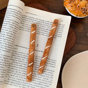 Close-up of cute baguette-shaped ceramic stirrers with smiley faces on a book