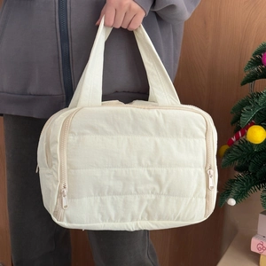 Detail of cream quilted makeup bag featuring side zippers and durable top handle strap