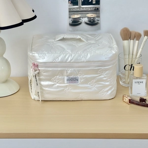 Close-up of quilted cream PU makeup bag featuring 3D bow texture and pink zipper detail