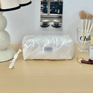 Detailed view of white quilted cosmetic bag with butterfly pattern on wooden desk