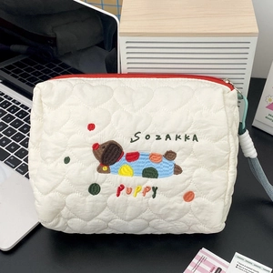 Detail of cream quilted makeup bag with colorful puppy embroidery and red zipper