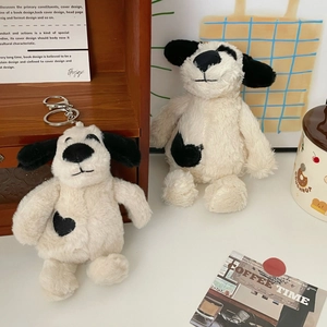 Cute plush puppy keychain with black heart patch and soft cream fur on wooden shelf