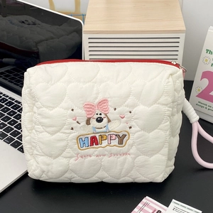 Detail of white quilted makeup bag featuring cartoon dog embroidery and red zipper closure