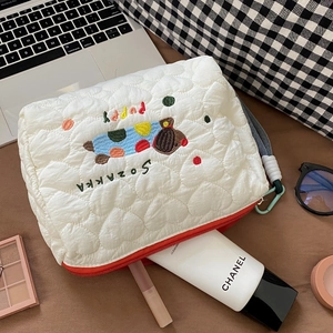 Quilted white cosmetic bag with dog embroidery and colorful dots on a wooden desk