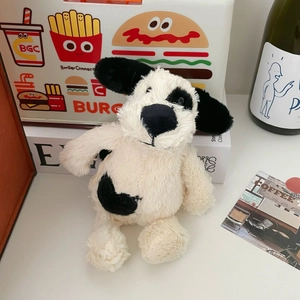 Close-up of soft black and white spotted puppy plush keychain on a minimalist desk