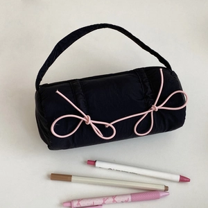 Quilted black cylinder pencil case with pink bow and handle shown with pens for size