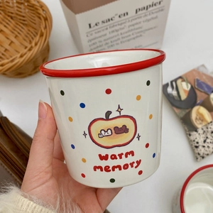 Detail of white ceramic apple mug with red rim and colorful polka dots in a cozy home setting