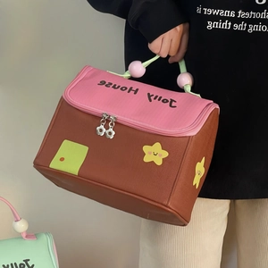 Close-up of a house-shaped lunch bag with pink roof, green handle and floral zippers
