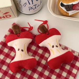 Detailed view of two plush apple core charms with smiling faces on a picnic cloth