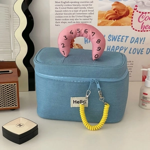 Detail of blue denim cosmetic bag featuring pink crescent handle and yellow spiral lanyard