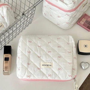 Detail of white quilted makeup bag with pink bow prints and brand logo label