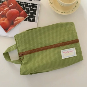 Close-up of green checkered travel organizer bag with zipper and logo label on a desk