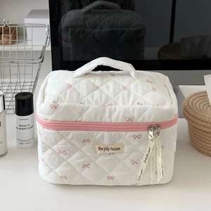 Close-up of quilted white makeup bag with pink bow pattern and ribbon zipper detail