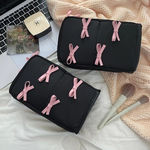 Detail of black makeup bag with pink 3D bows and cosmetics on a warm desktop