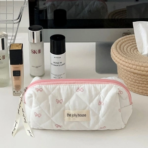 Detailed shot of white quilted makeup bag featuring pink bow embroidery and ribbon