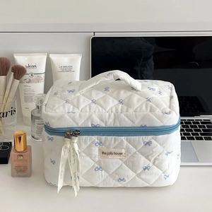 Détail de la trousse à maquillage blanche matelassée avec nœuds bleus et ruban de zip