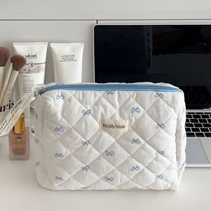 Détail d'une trousse de maquillage matelassée blanche avec motifs de nœuds bleus