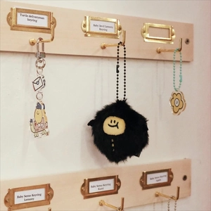 Detail view of plush demon and turtle messenger keychains hanging on a wood display board