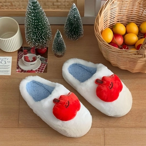 Pantoufles d'hiver en peluche avec motif pomme rouge et doublure bleue sur sol en bois
