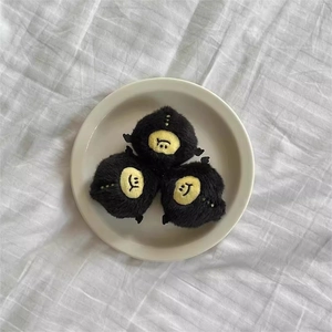 Three cute black plush monster charms with yellow faces displayed on a white plate
