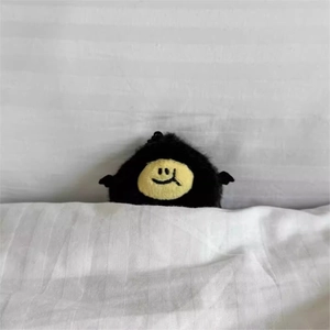 Close-up of cute black plush devil lemon pendant peeping from white bedding sheets