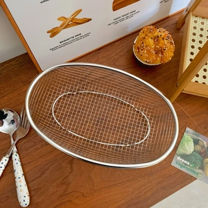 Detailed view of an oval stainless steel mesh basket on a rustic wooden dining table