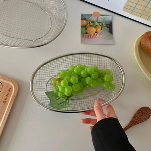 Detailed view of an oval stainless steel mesh basket holding fresh green grapes for washing