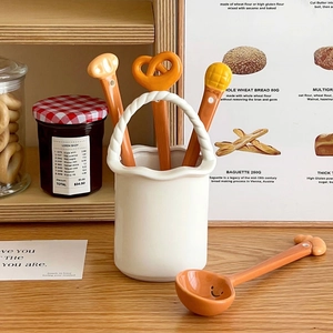Detail view of 4 ceramic bread-shaped spoons with a matching woven-texture storage jar