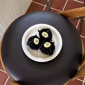 Three fuzzy black monster plush keychains with yellow smiling faces on white plate