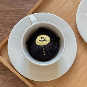 Close-up of cute black plush demon lemon charm resting in a white ceramic coffee cup