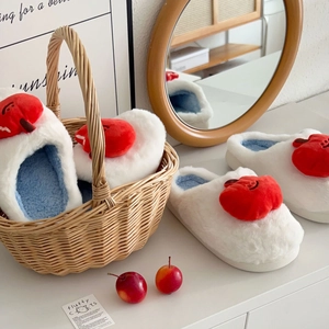Détail d'un chausson blanc en peluche avec un pomme rouge décorative et un sourire