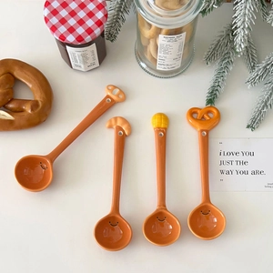 Four orange ceramic spoons with bread-shaped handles and smiley faces on a white background
