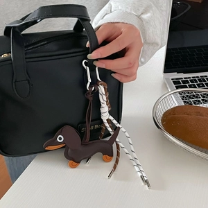 Brown leather dachshund charm attached to a black textured tote bag with silver clip