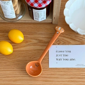 Detail of a long handle ceramic spoon with an orange cat paw design and a cute smiley face
