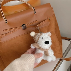 Detail of white plush puppy keychain with brown knitted hat on a suede handbag