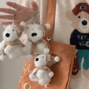 Close-up of plush white puppy keychain with brown knitted hat and silver keyring