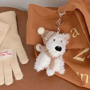 Detail of white plush puppy keychain with brown knitted hat on a canvas bag