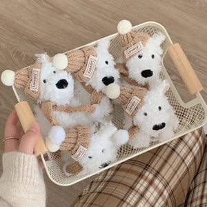 White plush dog keychains with brown knit hats and scarves in a decorative metal basket