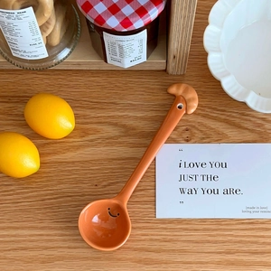 Macro shot of orange ceramic spoon with a smiley face and 3D croissant shaped handle