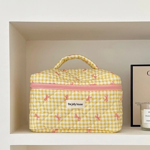 Detail of yellow checkered quilted makeup bag with pink bow embroidery and top handle