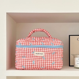 Close-up of quilted red and white checkered makeup bag with blue bow prints and hand strap