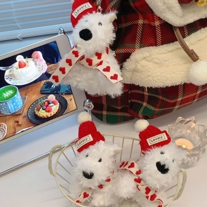 Close-up of white plush dog keychain with red Christmas hat and heart scarf on a cozy bag