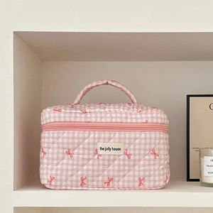 Pink and white checkered quilted makeup bag featuring a bow and top handle on a shelf