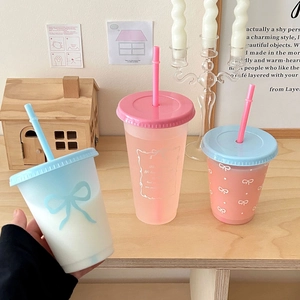 Three colorful plastic straw cups with cute bows on a wooden table in a cozy home setting