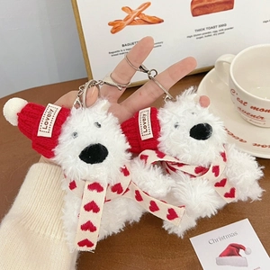 Cute white plush puppy keychain with red Christmas hat and scarf on a cozy background