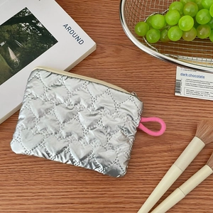 Close-up of heart-quilted silver coin purse with vibrant pink woven zipper pull detail