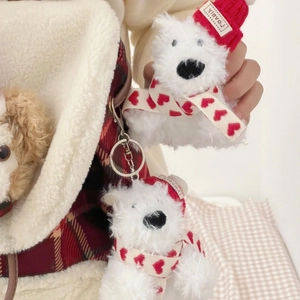 Close-up of white plush dog keychain with a red knit hat and heart-patterned scarf