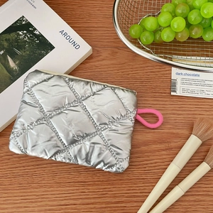 Close-up of silver quilted coin purse with metallic finish and pink lanyard on wood