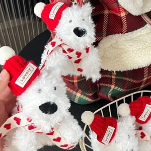Detail of plush white dog charm with red knit hat and heart scarf on plaid bag
