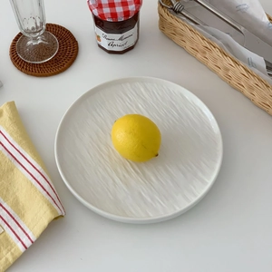 Top-down view of a white ceramic plate with rippled texture and a fresh lemon